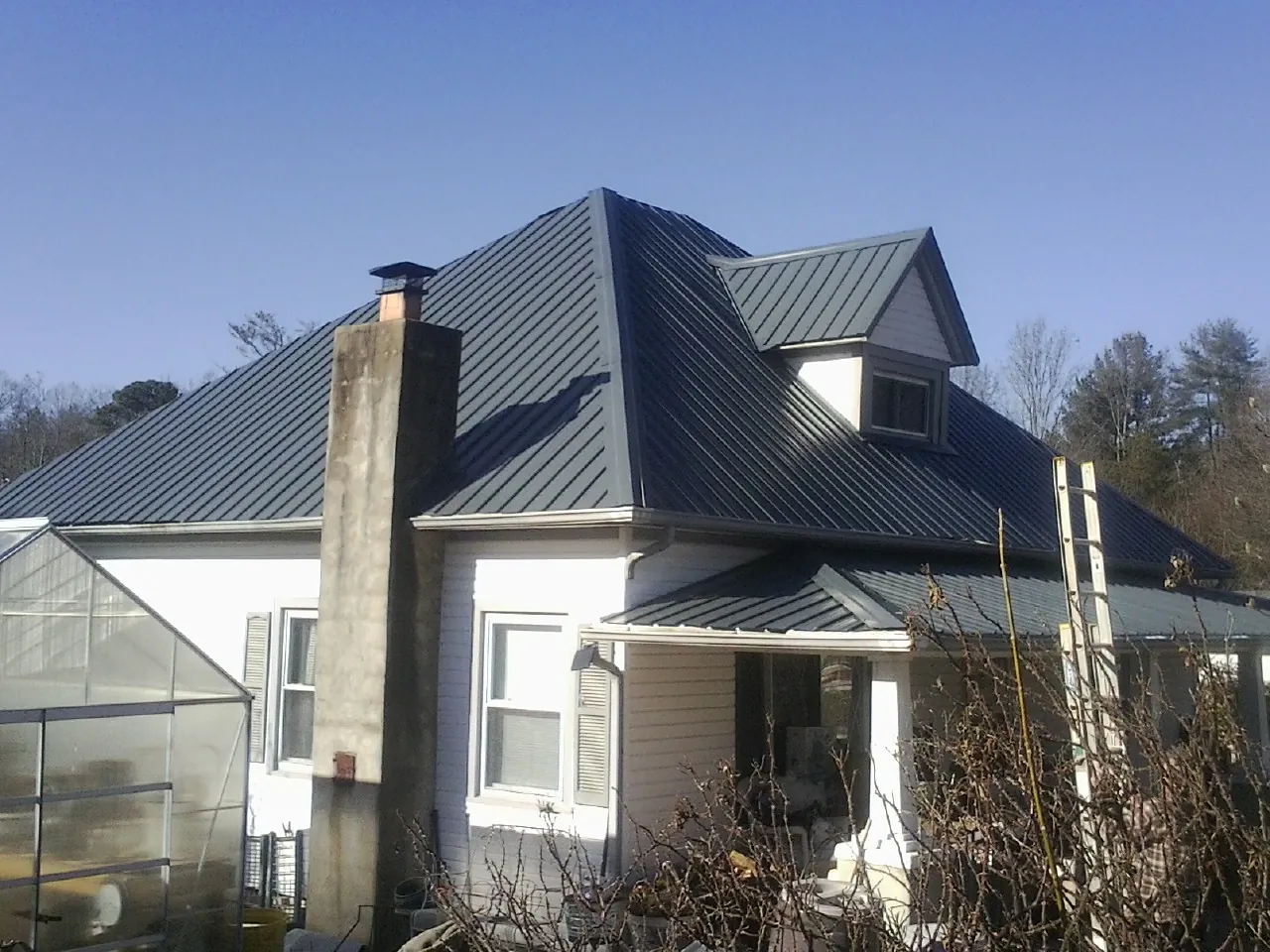 Dark blue standing seam metal roof on a white farmhouse with dormer — Slate & Tile Roof Repair by Roofing Brothers in Jonesburg