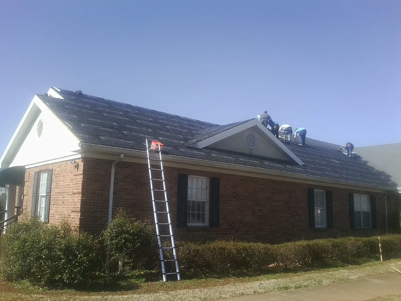 Crew tearing shingles off a brick ranch roof with a ladder set — Emergency Roof Repair work by our crew in Jonesburg