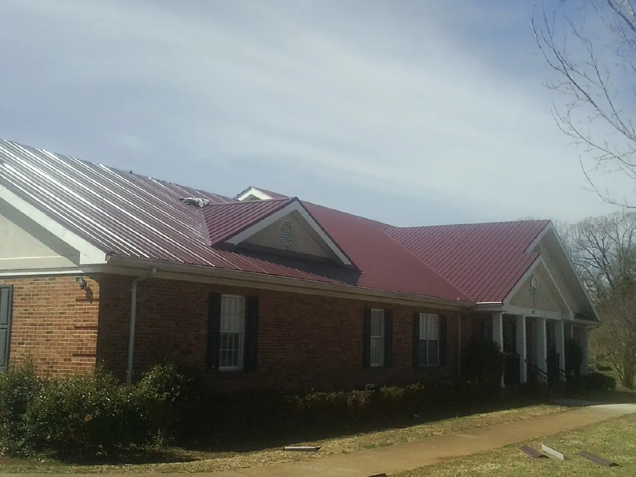 Red metal roof with gabled entries on a long brick building, from a Hail Damage Roof Repair job in Jonesburg