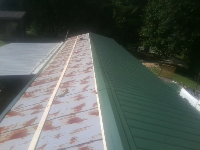Old rusted panels beside newly installed green metal roofing in Jonesburg