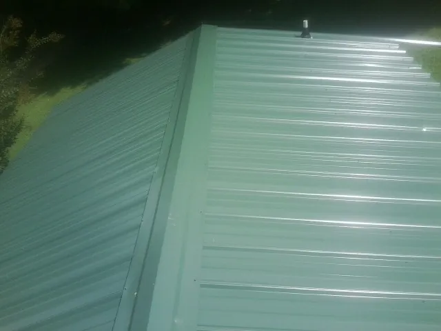 New green metal panels meeting at the ridge of a roof — Flat Roof Repair work by our crew in Jonesburg