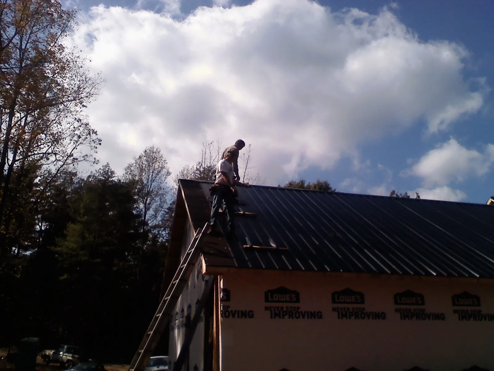Roofer fastening dark metal panels high against a cloudy sky, from a Roof Inspection job in Jonesburg