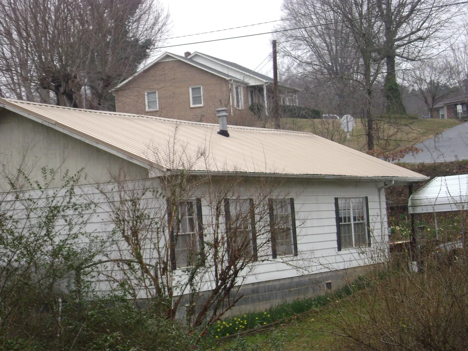 Tan metal roof on a white sided house set into a hillside — Commercial Roofing by Roofing Brothers in Jonesburg